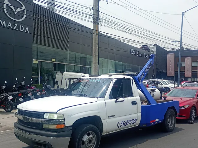 Grúa de arrastre entregando un auto rojo frente a una agencia automotriz