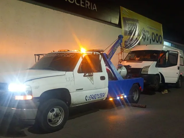 Grúa de Grúas Delta remolcando una van blanca de noche con la torreta encendida